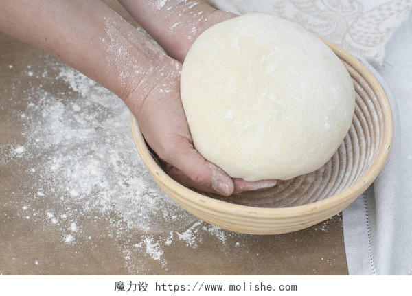 两个手拿着面包面团盖在木制桌子上的一个防腐篮子上用面粉在厨房